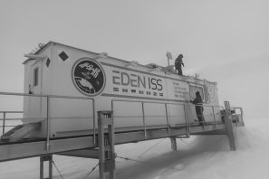 Ein Container steht auf einem gerüst in der Arktis und zwei Männer befestigen ein Netz