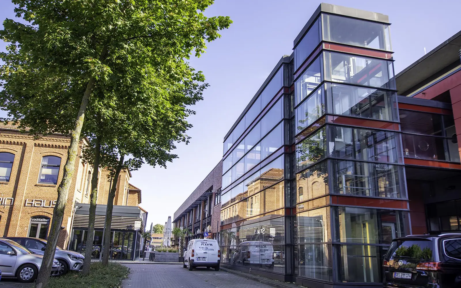 links Asuöäufer eines Industriegebäudes dem Ende des 18. Jahrhnderts und rechts eine moderne Glasfront mit Glasturm.